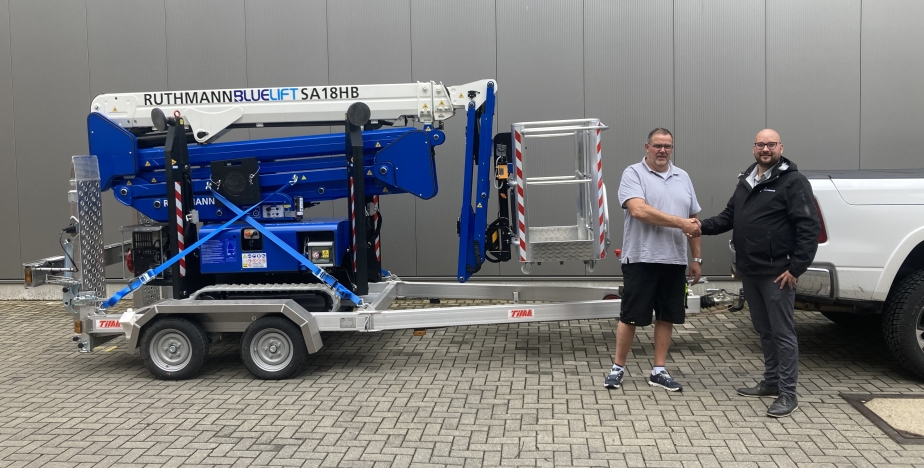 Sascha Schüttler (l.) freut sich über seine neue Raupenarbeitsbühne BLUELIFT SA 18 HB inkl. Transportanhänger, übergeben von Lukas Weigand (r., Sales Manager BLUELIFT, RUTHMANN)